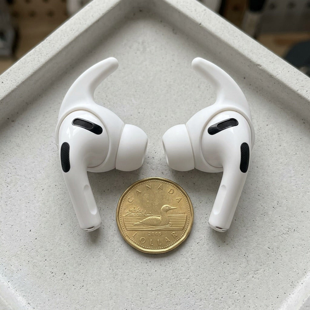 A photo of white KeyBudz ear covers for AirPods Pro 3rd Gen next to a Canadian loonie for scale.