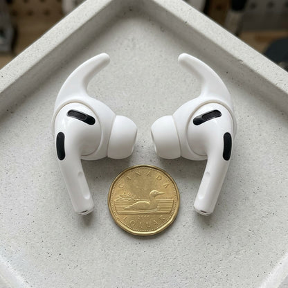 A photo of white KeyBudz ear covers for AirPods Pro 3rd Gen next to a Canadian loonie for scale.