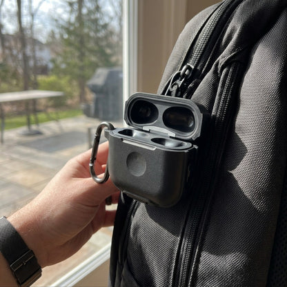 A KeyBudz ElementProof case for AirPods, in rugged carbon black silicone, clipped to a backpack zipper.